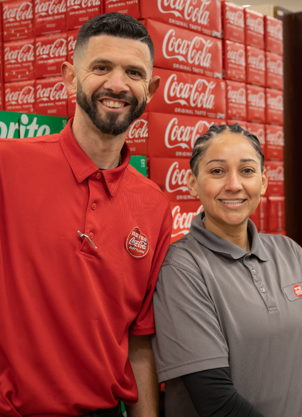 Smiling man and woman pose in uniform in front of a Coca-Cola display