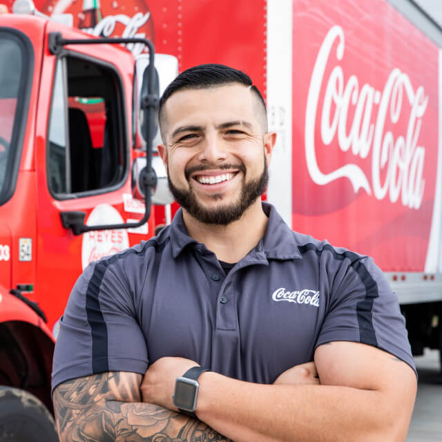 Smiling truck driver stands in front of Coca-Cola truck with arms crossed