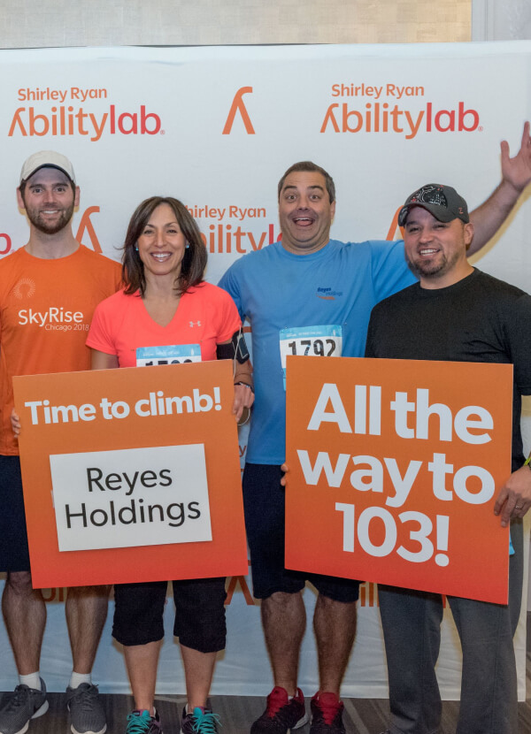 Four Reyes's employees wearing sport outfits and holding "Time to climb" and "all the way to 103!" posters