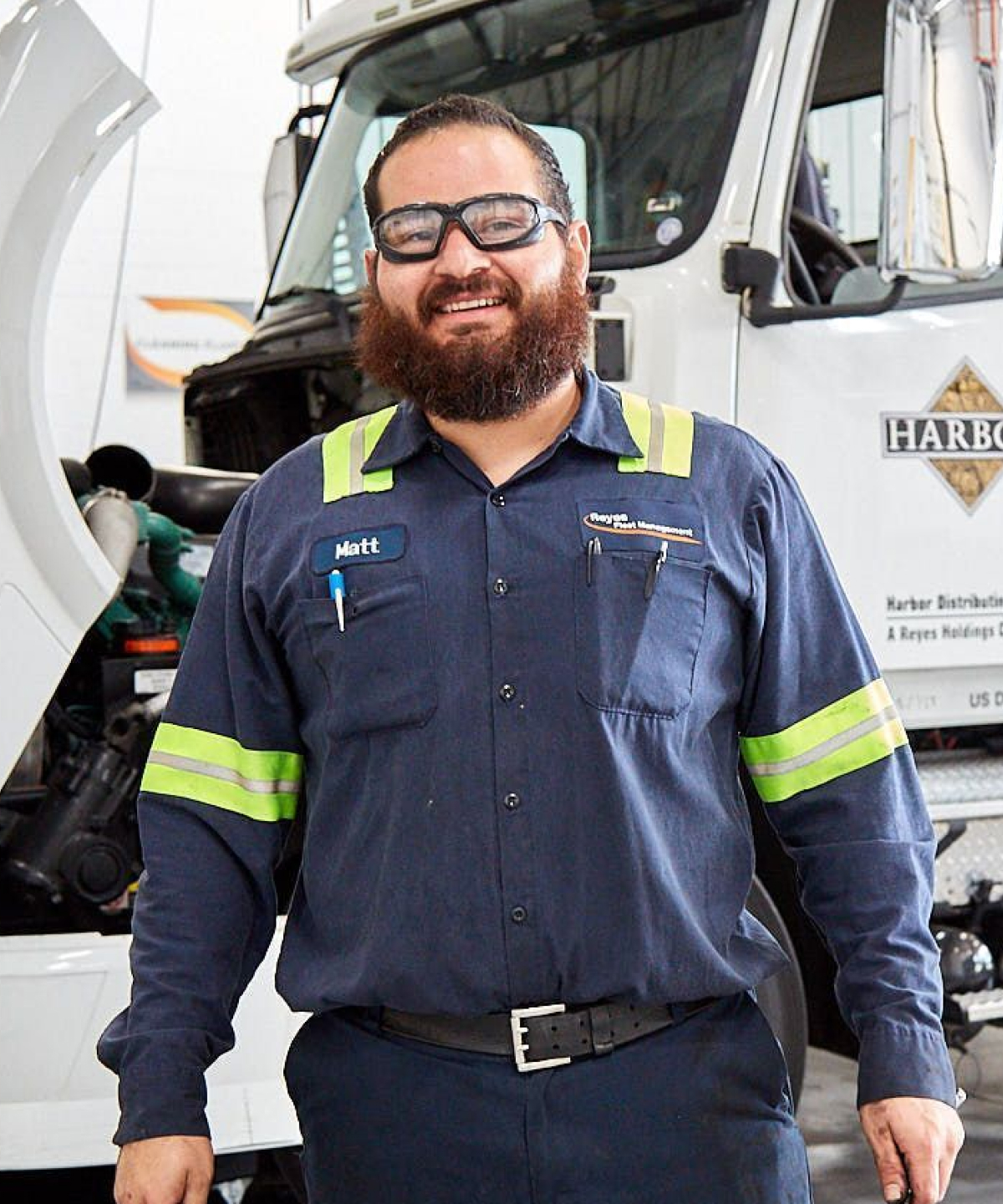 Smiling man wearing Reyes Fleet Management uniform standing in front of the truck