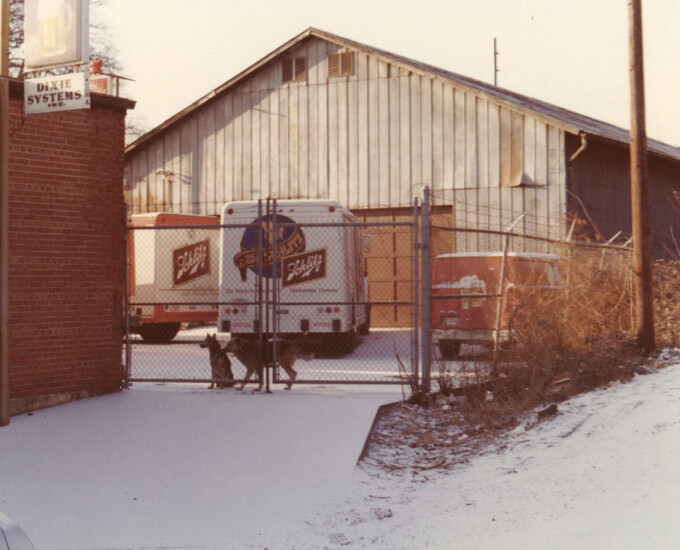 Vintage photo of Schlitz beer trucks parked behind chain link fence with two dogs guarding the lot