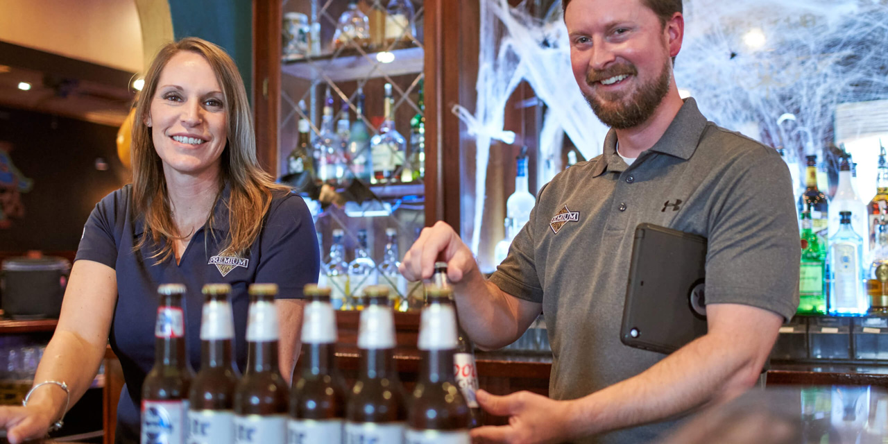 Man and woman smile behind bar while arranging Miller Lite bottles in customer account